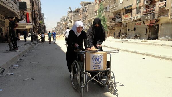 Residents of Syria's Yarmuk Palestinian refugee camp, south of Damascus, use a wheelchair to carry a box of goods distributed by the United Nations Relief and Works Agency (UNRWA) on July 17, 2014 - Sputnik International