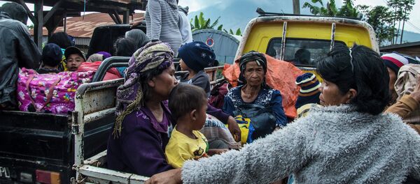 Residents are evacuated on farm vehicles at a village in the district of Karo near Mount Sinabung volcano, seen in the background, partly covered by clouds on June 3, 2015 - Sputnik International