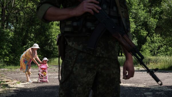 Woman walks with her child as Ukrainian serviceman stands guard on June 8, 2015 in Novotoshkivske village, Donetsk region - Sputnik International