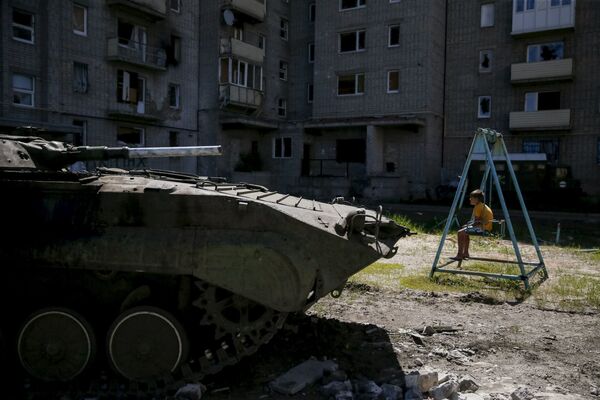 A boy sits on a swing near a building, which was damaged during fighting between Kiev and Donbass forces, as an armoured personnel carrier (APC) of the Ukrainian armed forces is seen nearby in Avdeyevka near Donetsk. June 7, 2015. A boy sits on a swing near a building, which was damaged during fighting between Kiev and Donbass forces, as an armoured personnel carrier (APC) of the Ukrainian armed forces is seen nearby in Avdeyevka near Donetsk. June 7, 2015. - Sputnik International