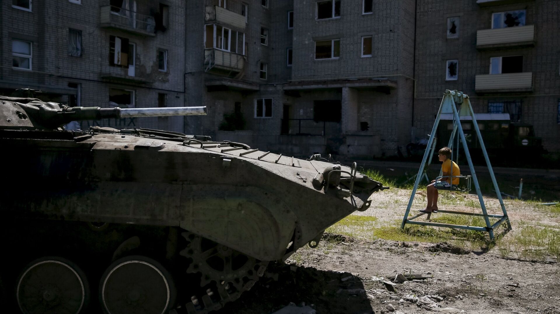 A boy sits on a swing near a building, which was damaged during fighting between Kiev and Donbass forces, as an armoured personnel carrier (APC) of the Ukrainian armed forces is seen nearby in Avdeyevka near Donetsk. June 7, 2015. - Sputnik International, 1920, 28.02.2022