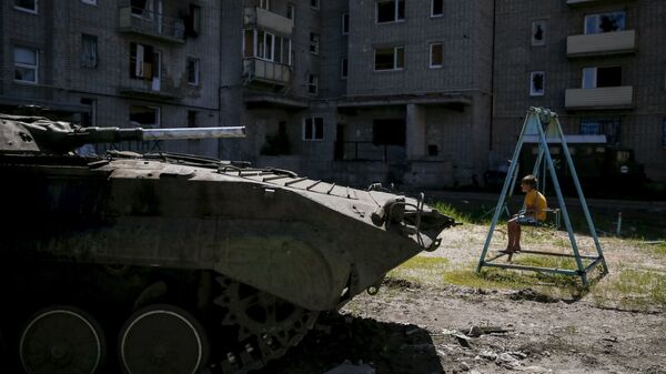 A boy sits on a swing near a building, which was damaged during fighting between Kiev and Donbass forces, as an armoured personnel carrier (APC) of the Ukrainian armed forces is seen nearby in Avdeyevka near Donetsk. June 7, 2015. - Sputnik International