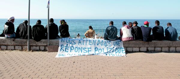 Migrants sit near a banner reading We are waiting fo a political response on the shores of the Mediterranean sea in the Italian Franco-Italian border city of Ventimiglia on June 15, 2015, as they wait to cross into France - Sputnik International