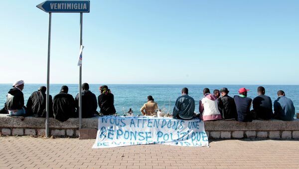 Migrants sit near a banner reading We are waiting fo a political response on the shores of the Mediterranean sea in the Italian Franco-Italian border city of Ventimiglia on June 15, 2015, as they wait to cross into France - Sputnik International