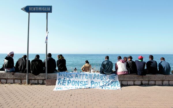 Migrants sit near a banner reading We are waiting fo a political response on the shores of the Mediterranean sea in the Italian Franco-Italian border city of Ventimiglia on June 15, 2015, as they wait to cross into France - Sputnik International