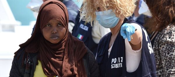 A forensic police officer gives indications to a woman as migrants arrived at Pozzallo's harbor near Ragusa, Sicily, Italy. A forensic police officer gives indications to a woman as migrants arrived at Pozzallo's harbor near Ragusa, Sicily, Italy. - Sputnik International