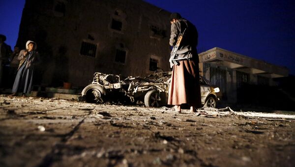 An armed man looks at the wreckage of a car at the site of a car bomb attack in Yemen's catpital Sanaa June 17, 2015 - Sputnik International