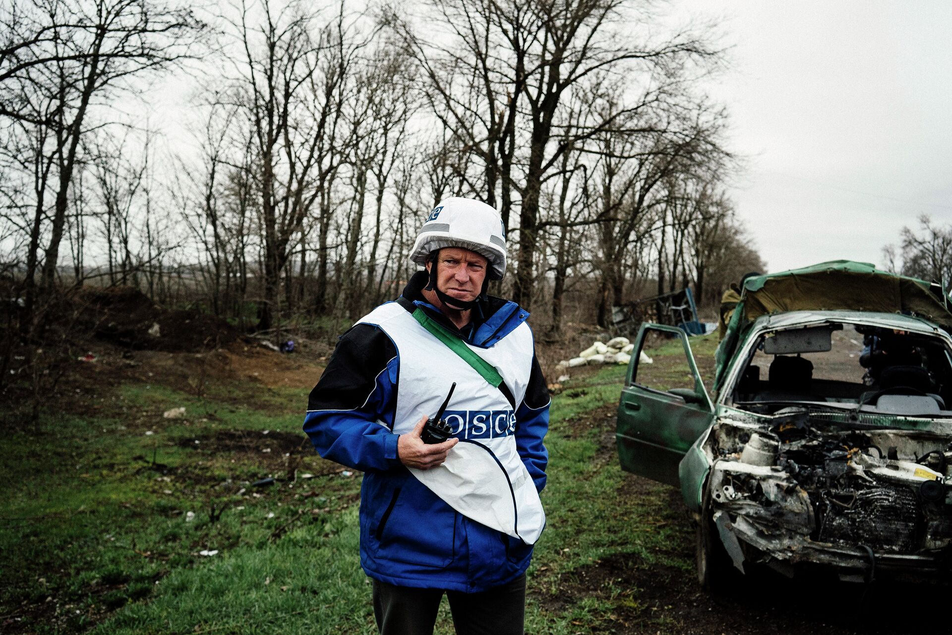 An International observer of the Organization for Security and Co-operation in Europe (OSCE) stands next to a destroyed car after shelling during an inspection tour near the village of Shirokino - Sputnik International, 1920, 01.12.2022