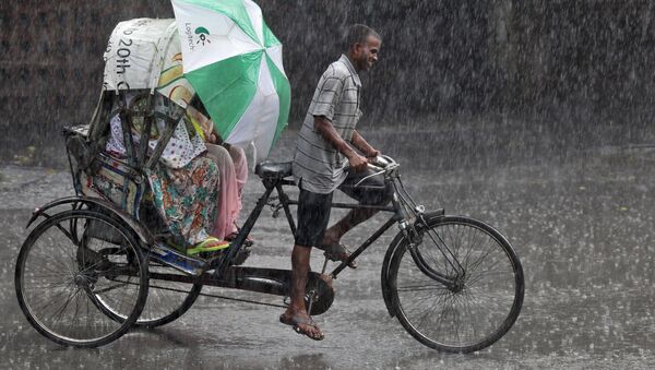 Commuters use an umbrella to protect themselves from a heavy rain shower as they travel in a cycle rickshaw in Chandigarh, India - Sputnik International