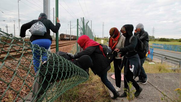 Migrants make their way across a fence near train tracks - Sputnik International