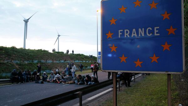 Migrants sit and block the road near a sign marked France in Coquelles, near Calais, France, July 30, 2015 - Sputnik International