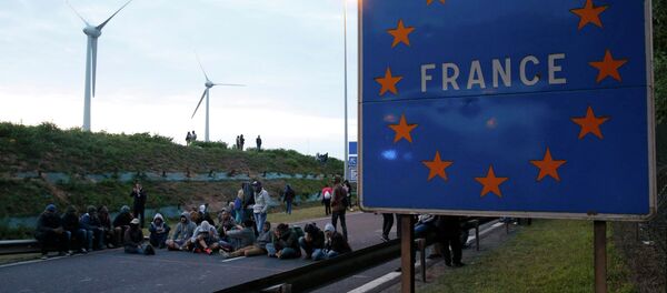 Migrants sit and block the road near a sign marked France in Coquelles, near Calais, France, July 30, 2015 - Sputnik International