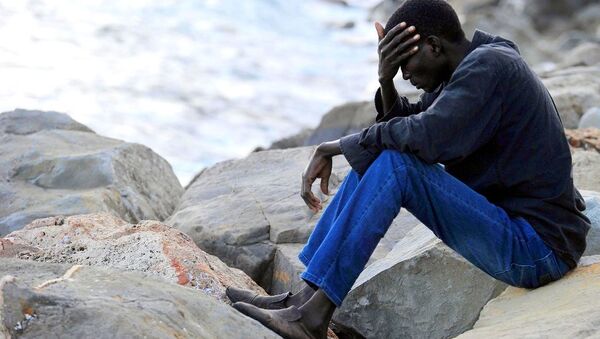 A migrant sits on rocks by the sea - Sputnik International