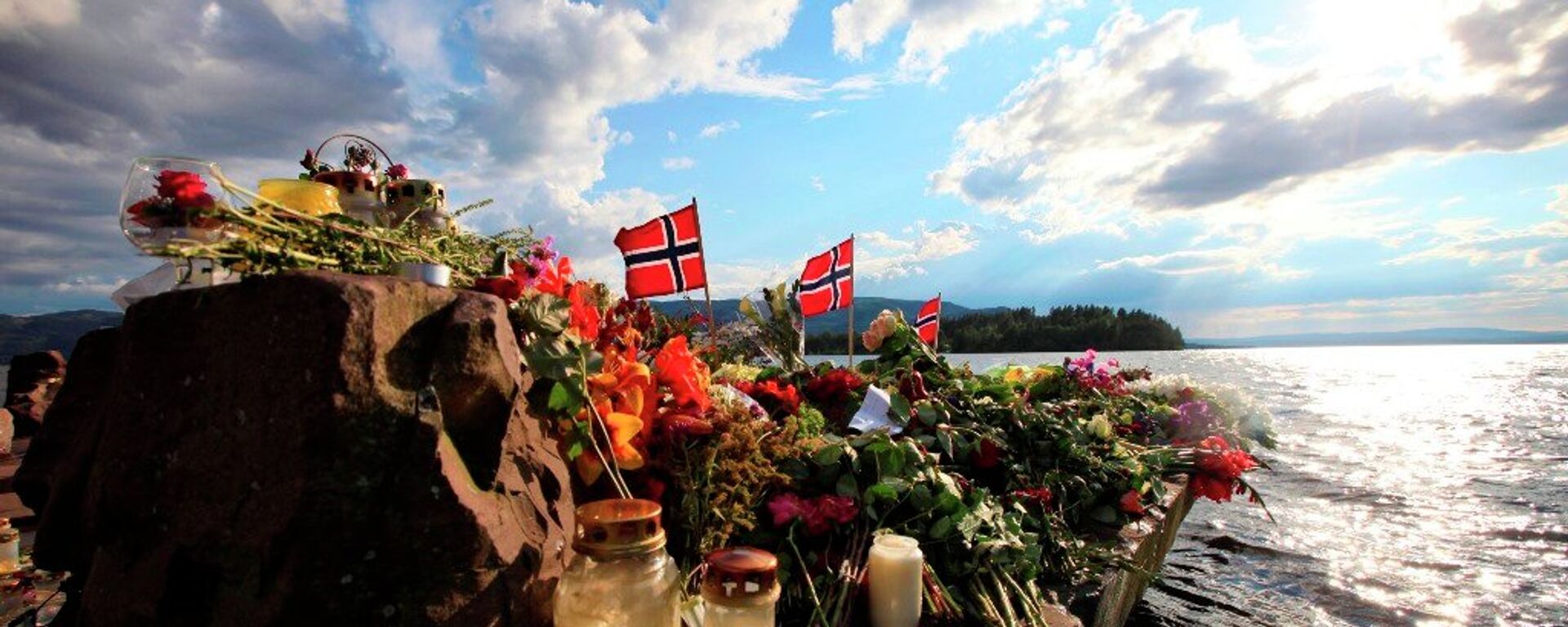 Norwegian flags and flowers are seen in Sundvollen, close to Utoya island, background, where gunman Anders Behring Breivik killed at least 68 people, near Oslo, Norway (Foto vom 28.07.11).  - Sputnik International, 1920, 21.07.2021