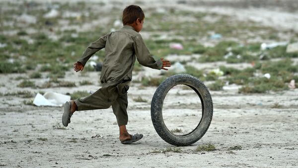 An Afghan Kochi nomad boy plays with a tire outside his tent on the outskirts of Kabul on August 2, 2015 - Sputnik International