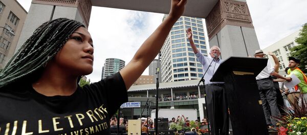 Mara Jacqueline Willaford, left, holds her fist overhead as Democratic presidential candidate Sen. Bernie Sanders, I-Vt., waves to greet the crowd before speaking at a rally Saturday, Aug. 8, 2015, in downtown Seattle. Mara Jacqueline Willaford, left, holds her fist overhead as Democratic presidential candidate Sen. Bernie Sanders, I-Vt., waves to greet the crowd before speaking at a rally Saturday, Aug. 8, 2015, in downtown Seattle. - Sputnik International