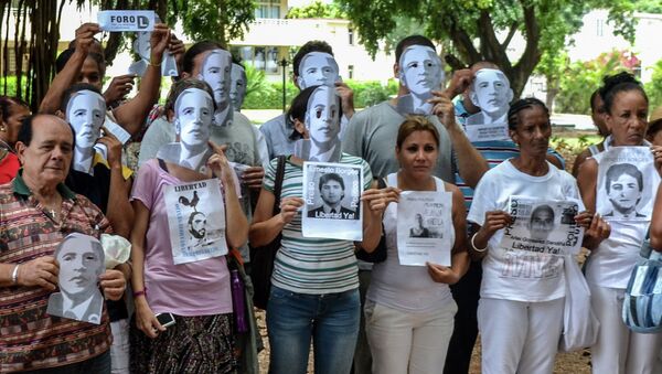 Cuban dissidents pose wearing masks depicting US President Barack Obama and holding pictures of imprisoned dissidents as they protest against the reopening of the US embassy in the island, during a meeting of the Ladies in White human rights group in a park of Havana, on August 9, 2015 - Sputnik International