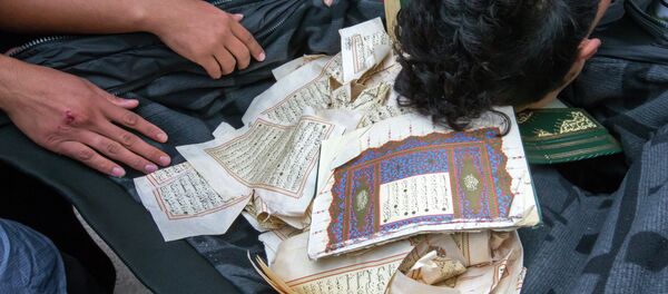 Refugees bow over ripped out pages from a Koran in a first registration center for refugees in Suhl, eastern Germany, on August 20, 2015 - Sputnik International