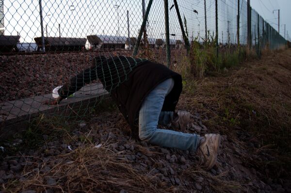 A migrant crawls under a fence as he attempts to access the Channel Tunnel in Calais, northern France, Saturday, Aug. 8, 2015 A migrant crawls under a fence as he attempts to access the Channel Tunnel in Calais, northern France, Saturday, Aug. 8, 2015 - Sputnik International