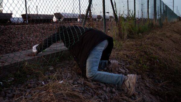 A migrant crawls under a fence as he attempts to access the Channel Tunnel in Calais, northern France, Saturday, Aug. 8, 2015 - Sputnik International