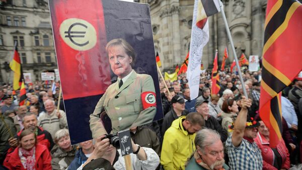 Supporters of the German right-wing movement PEGIDA (Patriotic Europeans Against the Islamisation of the Occident) hold up a poster showing German Chancellor Angela Merkel in a uniform with an Euro-logo-armband as they attend a PEGIDA rally on June 1, 2015 in Dresden, eastern Germany. - Sputnik International