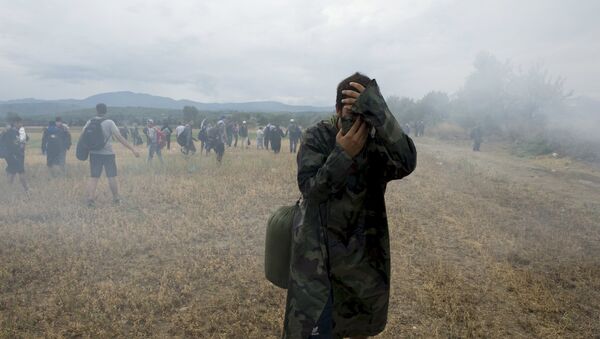 A migrant covers his face to avoid inhaling tear gas while others flee, as Macedonian police special forces block them from entering Macedonia on Greece's, near the village of Idomeni, Greece, August 22, 2015. - Sputnik International
