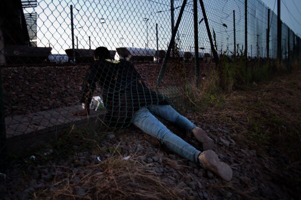 A migrant crawls under a fence as he attempts to access the Channel Tunnel in Calais, northern France, Saturday, Aug. 8, 2015. Some thousands of migrants have been crossing fence border controls near the Channel Tunnel linking France and Britain, trying to board freight trains or trucks destined for Britain A migrant crawls under a fence as he attempts to access the Channel Tunnel in Calais, northern France, Saturday, Aug. 8, 2015. Some thousands of migrants have been crossing fence border controls near the Channel Tunnel linking France and Britain, trying to board freight trains or trucks destined for Britain - Sputnik International