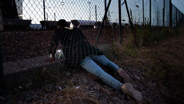 A migrant crawls under a fence as he attempts to access the Channel Tunnel in Calais, northern France, Saturday, Aug. 8, 2015. Some thousands of migrants have been crossing fence border controls near the Channel Tunnel linking France and Britain, trying to board freight trains or trucks destined for Britain - Sputnik International