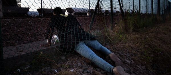 A migrant crawls under a fence as he attempts to access the Channel Tunnel in Calais, northern France, Saturday, Aug. 8, 2015. Some thousands of migrants have been crossing fence border controls near the Channel Tunnel linking France and Britain, trying to board freight trains or trucks destined for Britain - Sputnik International