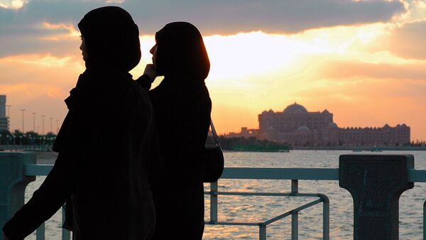 Two women walk along the Corniche in Abu Dhabi as the sun sets behind the Emirates Palace in the background. - Sputnik International