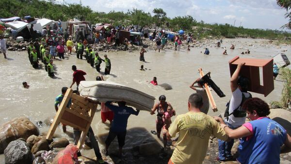 People carry their household belongings across the Tachira River from Venezuela, foreground, to Colombia, near San Antonio del Tachira, Venezuela, Tuesday, Aug. 25, 2015, during a mass exodus of Colombians living on the Venezuelan side of the border - Sputnik International
