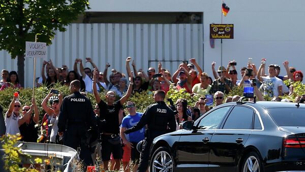 People hold a placard reading Traitor as German Chancellor Angela Merkel leaves after her visit to an asylum seekers accomodation facility in the eastern German town of Heidenau near Dresden, August 26, 2015 where last week more than 30 police were injured in clashes, when a mob of several hundred people pelted officers with bottles and fireworks - Sputnik International