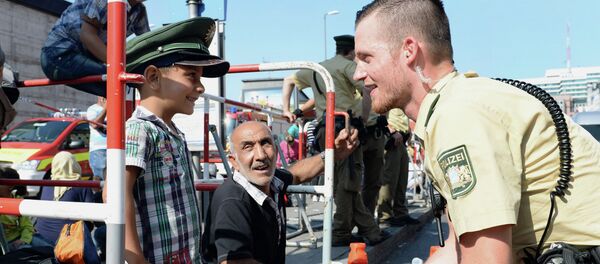German police officer and a migrant boy joke with the officer's cap while migrants wait for a bus after their arrival at the main train station in Munich, southern Germany, September 1, 2015 - Sputnik International