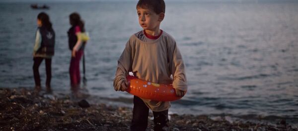 A Syrian migrant boy still wearing a swimming ring stands on the beach upon his arrival with other migrants by a dinghy at the southeastern Greek island of Kos, Greece, early Thursday, Aug. 20, 2015. - Sputnik International