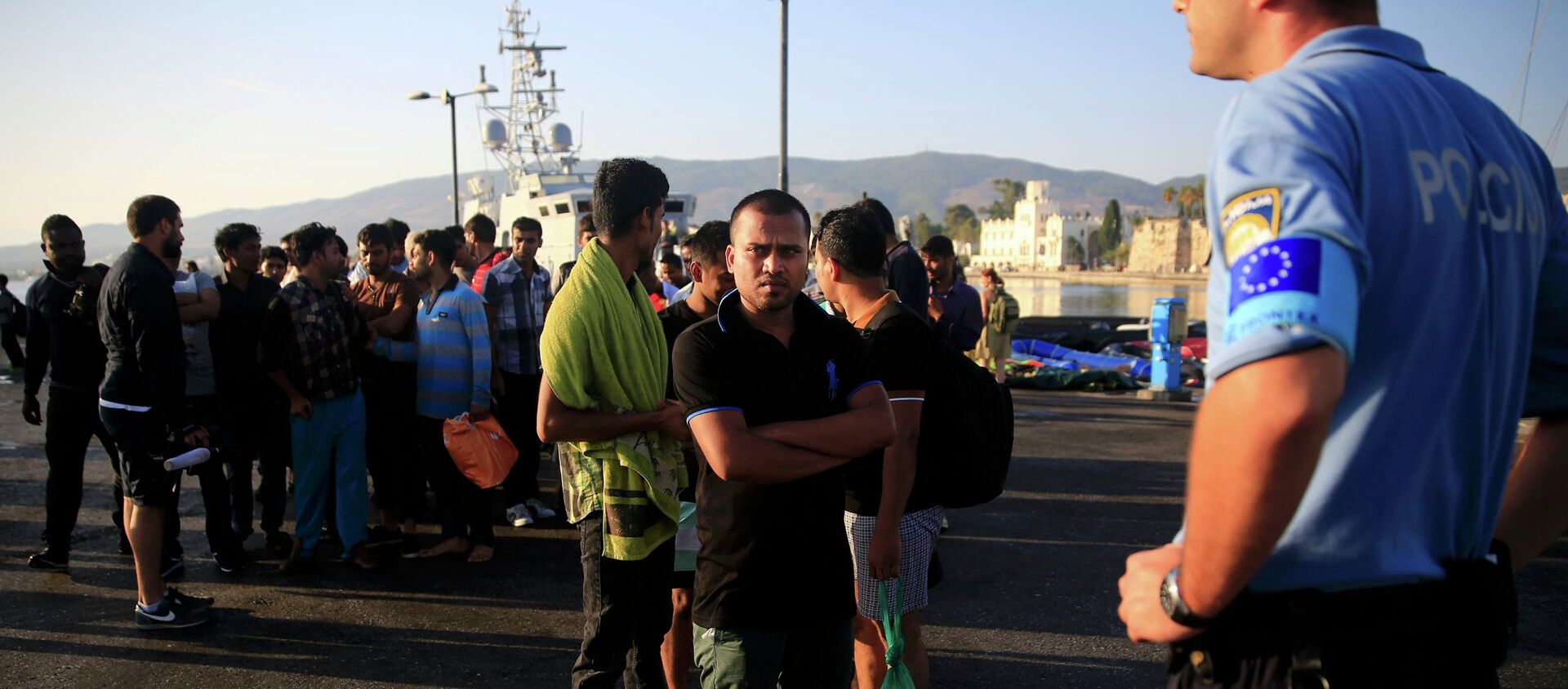 A migrant waits in line next to a Frontex officer (R) at the port of Kos, following a rescue operation off the Greek island of Kos, August 14, 2015 - Sputnik International, 1920, 02.11.2018
