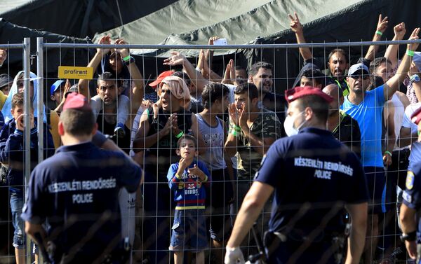 Migrants watch from behind a fence as Hungarian riot police stands guard in front of a migrant reception centre in Roszke, Hungary, September 4, 2015 - Sputnik International