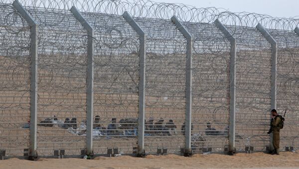 An Israeli soldier stands near the border fence between Israel and Egypt as African would-be immigrants sit on the other side near the Israeli village of Be'er Milcha, in this September 6, 2012 file photo - Sputnik International