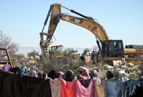 Palestinian women watch on as an Israeli army bulldozer with a demolition permit pulls down the house of the Palestinian Raba'ai family which Israeli authorities said was build without a permit, in Al-Dirat south of Yatta village near the West Bank town of Hebron on January 20, 2015.  - Sputnik International