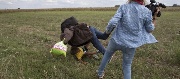 A refugee carrying a child falls after being tripped by a TV camerawoman while trying to escape from a collection point in Roszke village, Hungary. - Sputnik International
