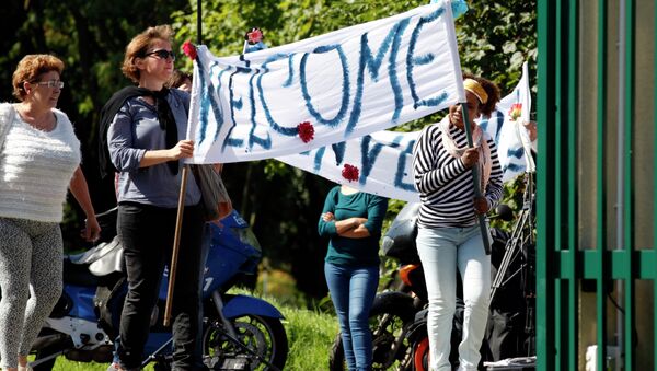 Neighbours hold a banner to cheer a group of migrants. - Sputnik International