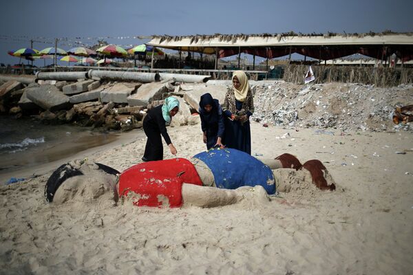 Palestinian girls put flowers on a sand sculpture by Indian artist Sudarsan Pattnaik depicting Syrian boy Alan Kurdi, a three-year-old boy who drowned off Turkey, on September 7, 2015, on Gaza city beach. Palestinian girls put flowers on a sand sculpture by Indian artist Sudarsan Pattnaik depicting Syrian boy Alan Kurdi, a three-year-old boy who drowned off Turkey, on September 7, 2015, on Gaza city beach. - Sputnik International