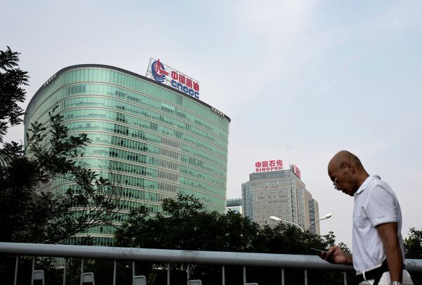 A man checks his mobile phone as he walks by buildings of China's state-owned companies, China National Offshore Oil Corp. (CNOOC), left, and China Petroleum & Chemical Corp. (Sinopec), in Beijing Monday, Sept. 14, 2015 A man checks his mobile phone as he walks by buildings of China's state-owned companies, China National Offshore Oil Corp. (CNOOC), left, and China Petroleum & Chemical Corp. (Sinopec), in Beijing Monday, Sept. 14, 2015 - Sputnik International
