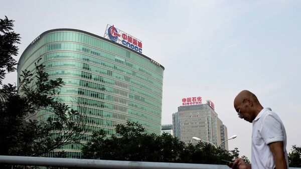 A man checks his mobile phone as he walks by buildings of China's state-owned companies, China National Offshore Oil Corp. (CNOOC), left, and China Petroleum & Chemical Corp. (Sinopec), in Beijing Monday, Sept. 14, 2015 - Sputnik International