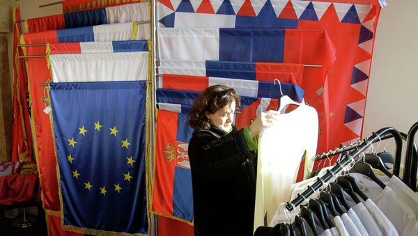 In this photo taken Wednesday, Dec. 7, 2011, a woman looks at an item of clothing in a shop as she stands next to a European Union flag and Serbian flags, in Belgrade, Serbia - Sputnik International