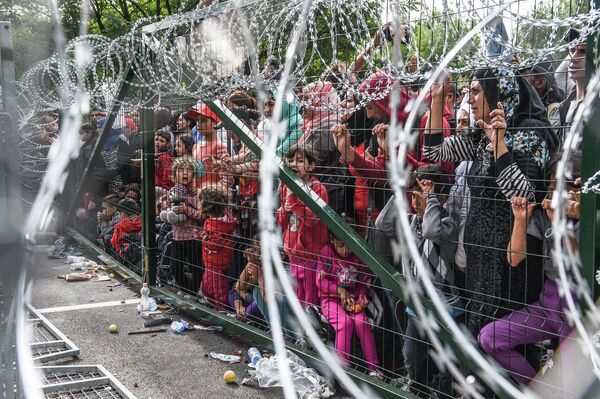Refugees stand behind a fence at the Hungarian border with Serbia near the town of Horgos on September 16, 2015 Refugees stand behind a fence at the Hungarian border with Serbia near the town of Horgos on September 16, 2015 - Sputnik International