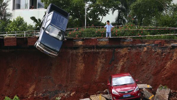 A man looks on as cars are seen stuck in a sinkhole that occurred in a parking area after heavy rainfall hit Haikou, Hainan province, China - Sputnik International