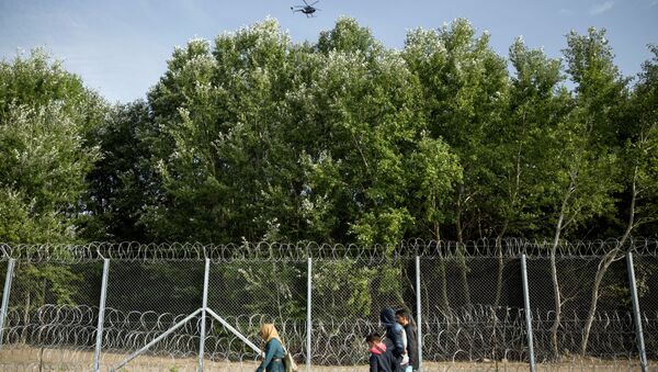 Migrants walk along the fence at the Serbian-Hungarian border while a helicopter flies over them near Horgos, Serbia,Tuesday, Sept. 15, 2015 - Sputnik International