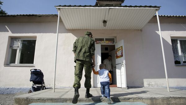 A man wearing a camouflage uniform walks with a child as they enter a school on the start of the new school year in Donetsk, Ukraine, September 1, 2015 - Sputnik International