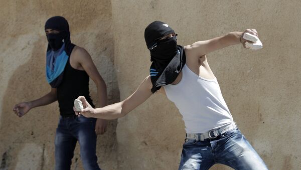 A masked Palestinian youth throws stones towards Israeli security forces during clashes - Sputnik International