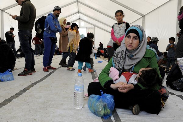 A migrant woman holds a baby inside a large tent set by NGOs, as refugees and migrants wait to cross Greece's border with Macedonia near the Greek village of Idomeni, September 26, 2015 - Sputnik International